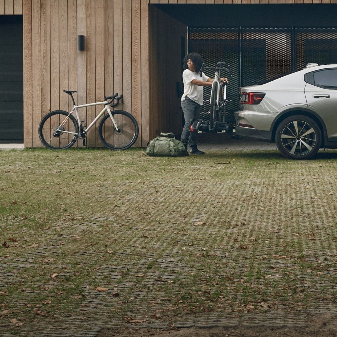 Een vrouw staat bij een Thule-trekstang die aan een auto is bevestigd, met één fiets erop geladen.