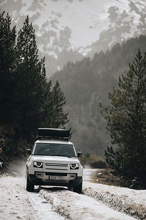 A vehicle driving down a snowy mountain road with a Thule Approach rooftop tent. 