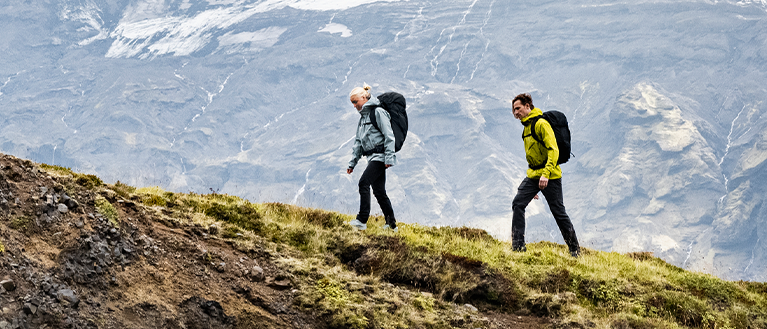 Dvoje ljudi hoda drvenom stazom u polju noseći Thule ruksake za planinarenje.