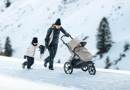 Förälder som skjuter en Thule-barnvagn genom snöiga förhållanden med ett barn som går bredvid dem.