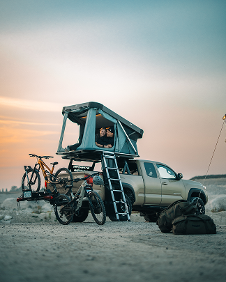 A mounted rooftop tent on a truck with a bike carrier on the back of the car.
