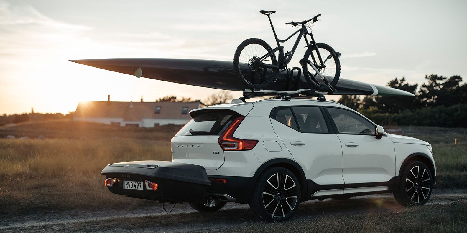A car driving down a road at sunset with a Thule Arcos cargo box on the back and Thule bike racks on the top carrying a surfboard and bike.