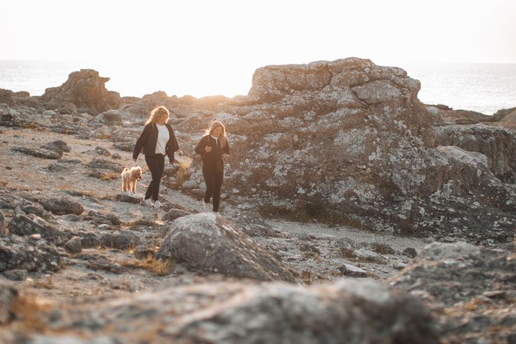 Two women are walking with their dog on a rocky beach.