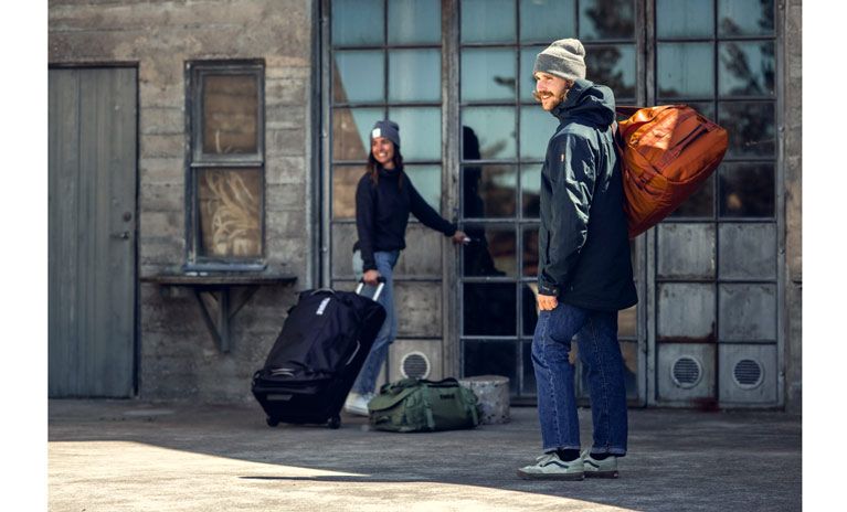 Two people look into the distance holding Thule Chasm duffel bags and check in luggage.