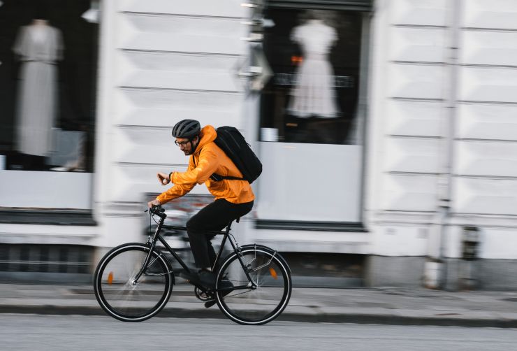 En mand cykler på en cykel med en Thule cykelrygsæk, mens han kigger på sit ur.