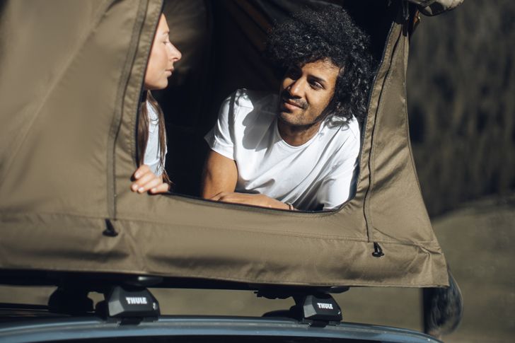 Mężczyzna i kobieta siedzą w namiocie na bagażniku bazowym Thule i patrzą na siebie.