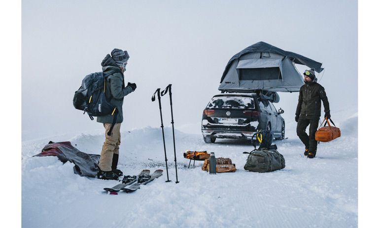 Two men stand in the snow with their car parked with a Thule rooftop tent.