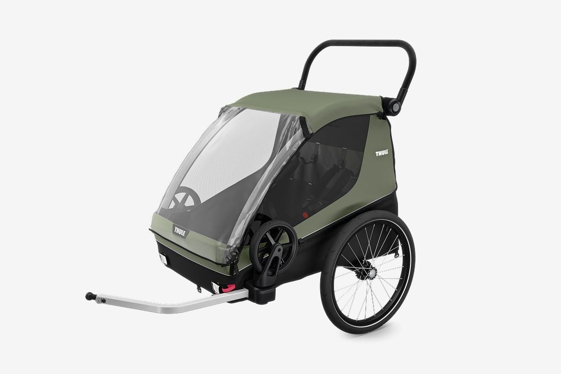 Un remolque verde de bicicletas Thule Courier para perros y carga se encuentra sobre un fondo gris claro. 