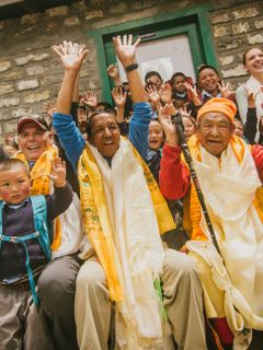 Apa Sherpa smiles and has his hands up while surrounded by smiling children and villagers.