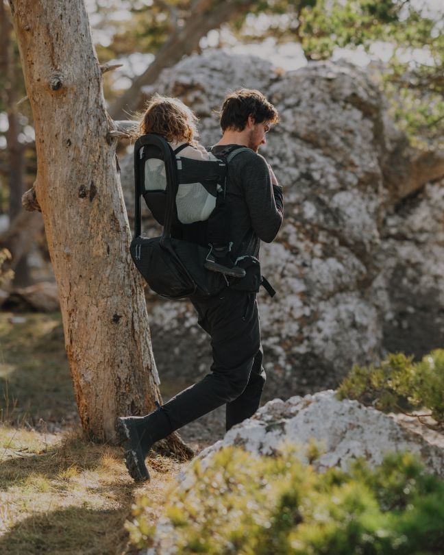 Une personne fait une randonnée dans la nature en portant un enfant dans un sac à dos porte-bébé Thule Sapling.