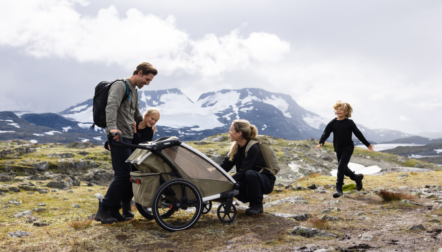 Familie udendørs med en cykeltrailer for børn i et bjerglandskab.