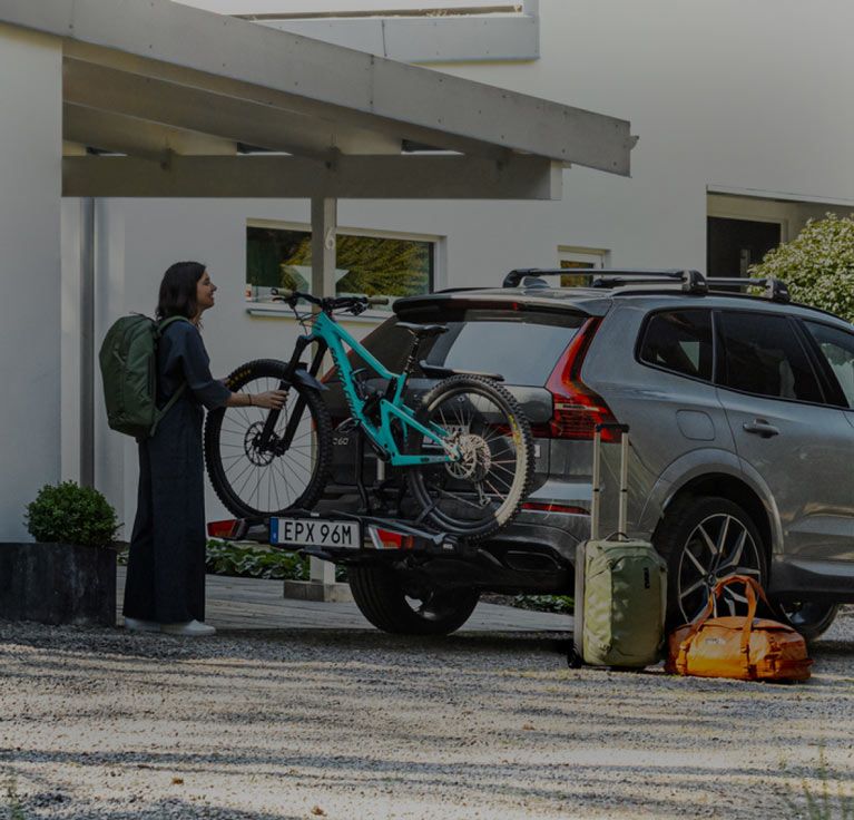 A woman unloads her bike from a Thule car bike rack as a man bikes away.