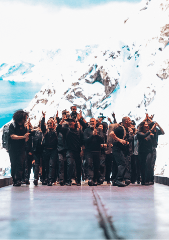 A group of people standing on a runway in front of a large screen displaying snowy mountain scenery, surrounded by an applauding audience.
