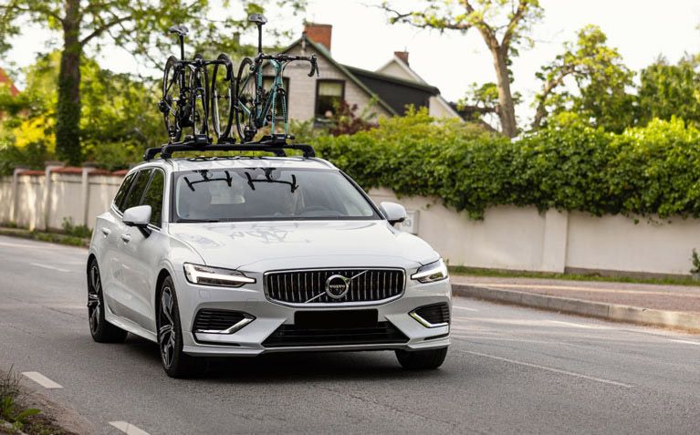 A car drives down a street with a Thule roof rack and a fork mount roof bike rack carrying two bicycles