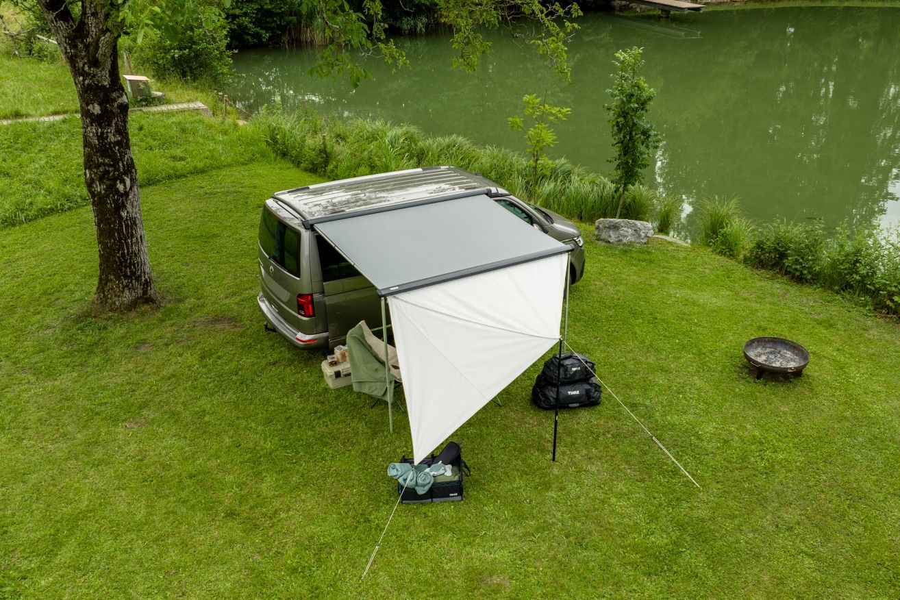 Van camper com painéis de toldo frontal Thule Subsola instalados em um acampamento à beira do lago.