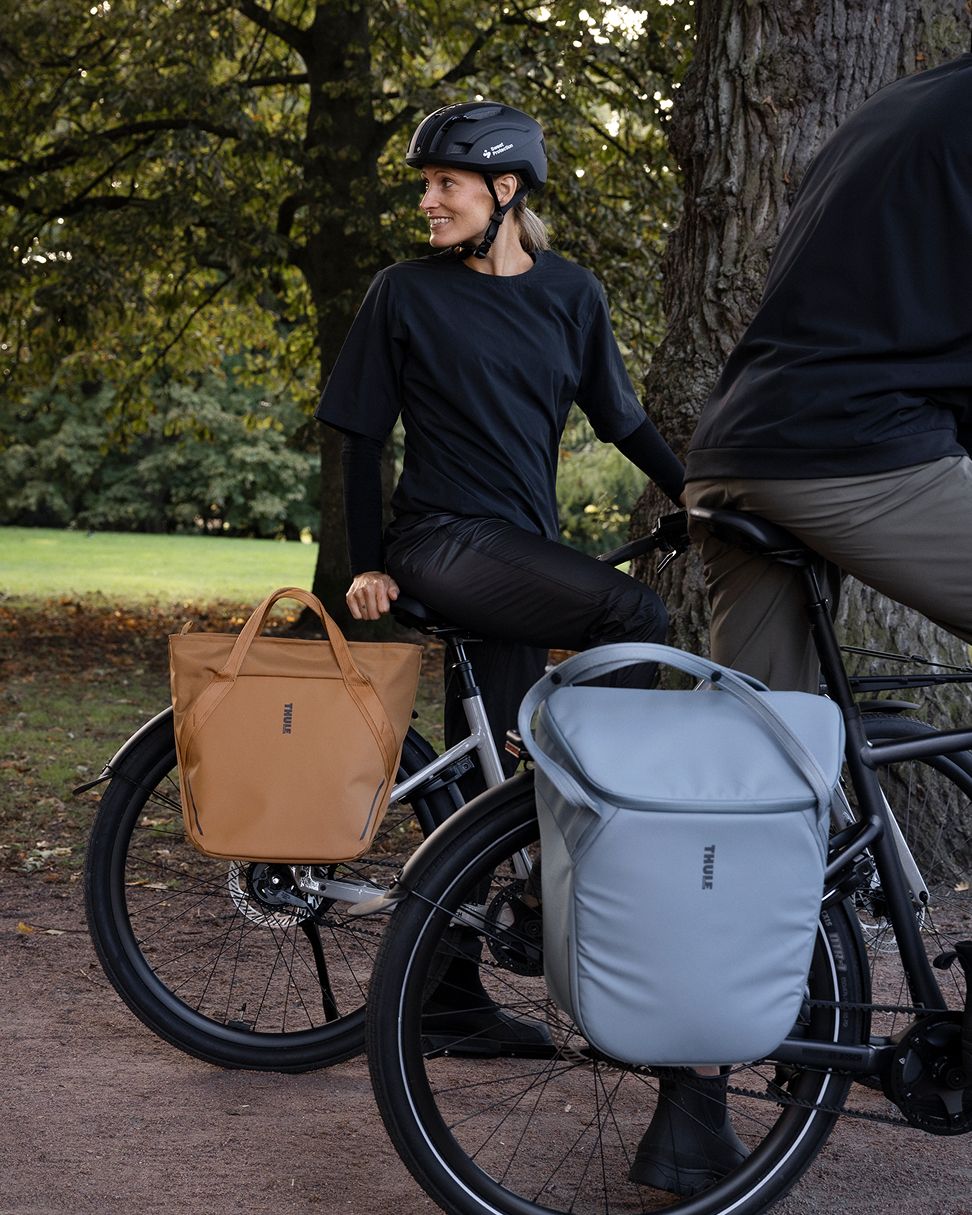 Duas pessoas com bicicletas pararam num caminho do parque, com grandes sacos de mala presos às bicicletas.