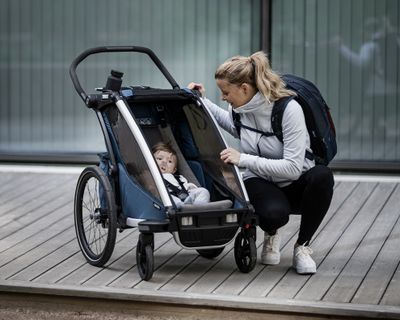 En kvinde kigger til sit barn inde i en cykeltrailer og et tilbehør til cykeltrailer.