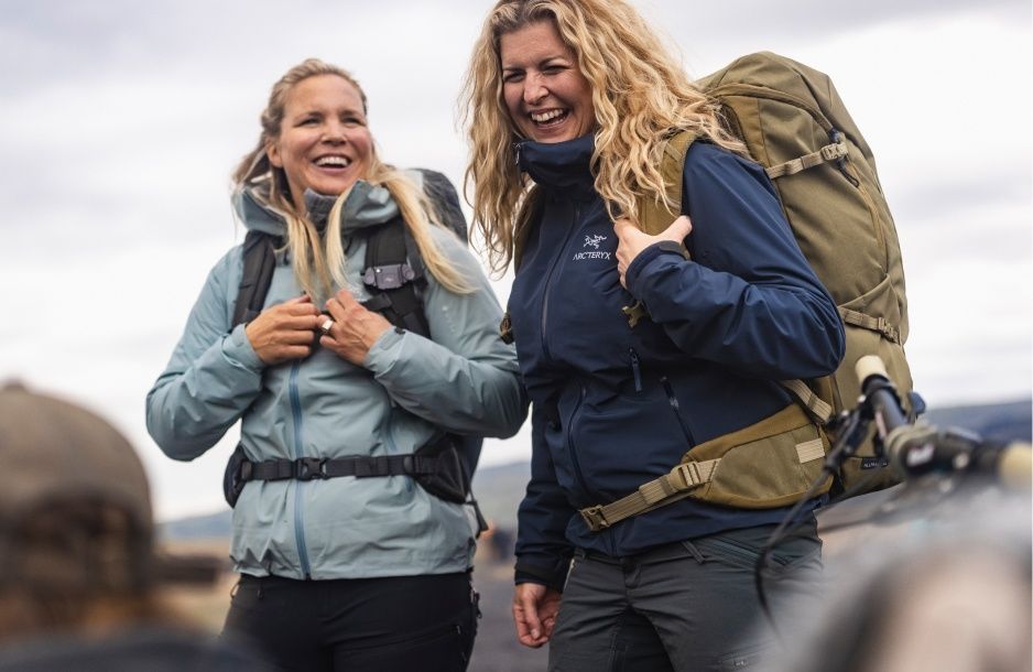 Two women laugh while hiking with Thule Alltrail hiking backpacks. 