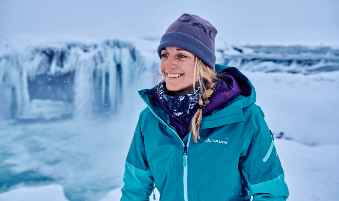 Aline Bock is smiling while wearing a coat and hat with snow in the background.