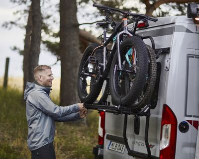 En man lastar cyklar på en cykelhållare på en husbil parkerad i skogen.