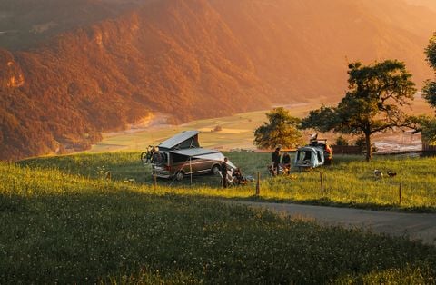 People sit in chairs next to two vehicles equipped with a Thule rooftop tents and Thule Outset hitch tent in nature.