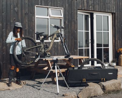 Велосипедист ремонтирует велосипед на специальной подставке, рядом стоит сумка для велоснаряжения.