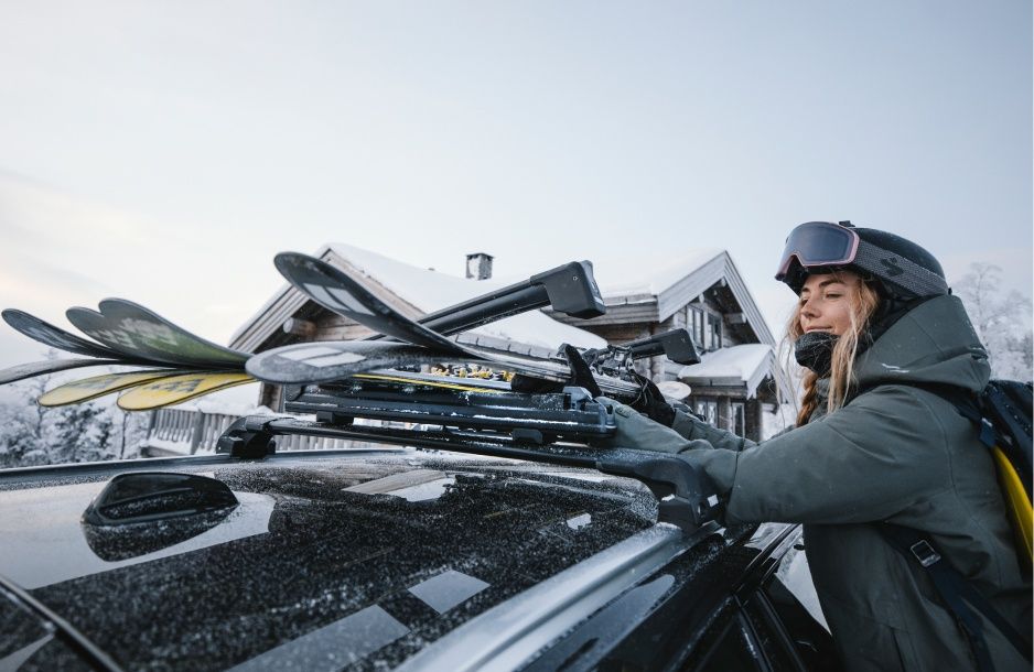 A woman loads her skis onto a vehicle with Thule Ski Racks on the roof.