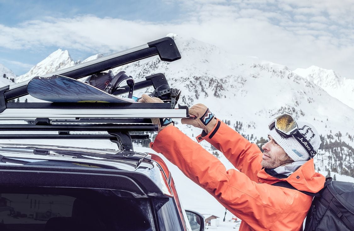 Thule Outlet hero banner showing a skier loading gear onto a roof rack in a snowy mountain landscape.