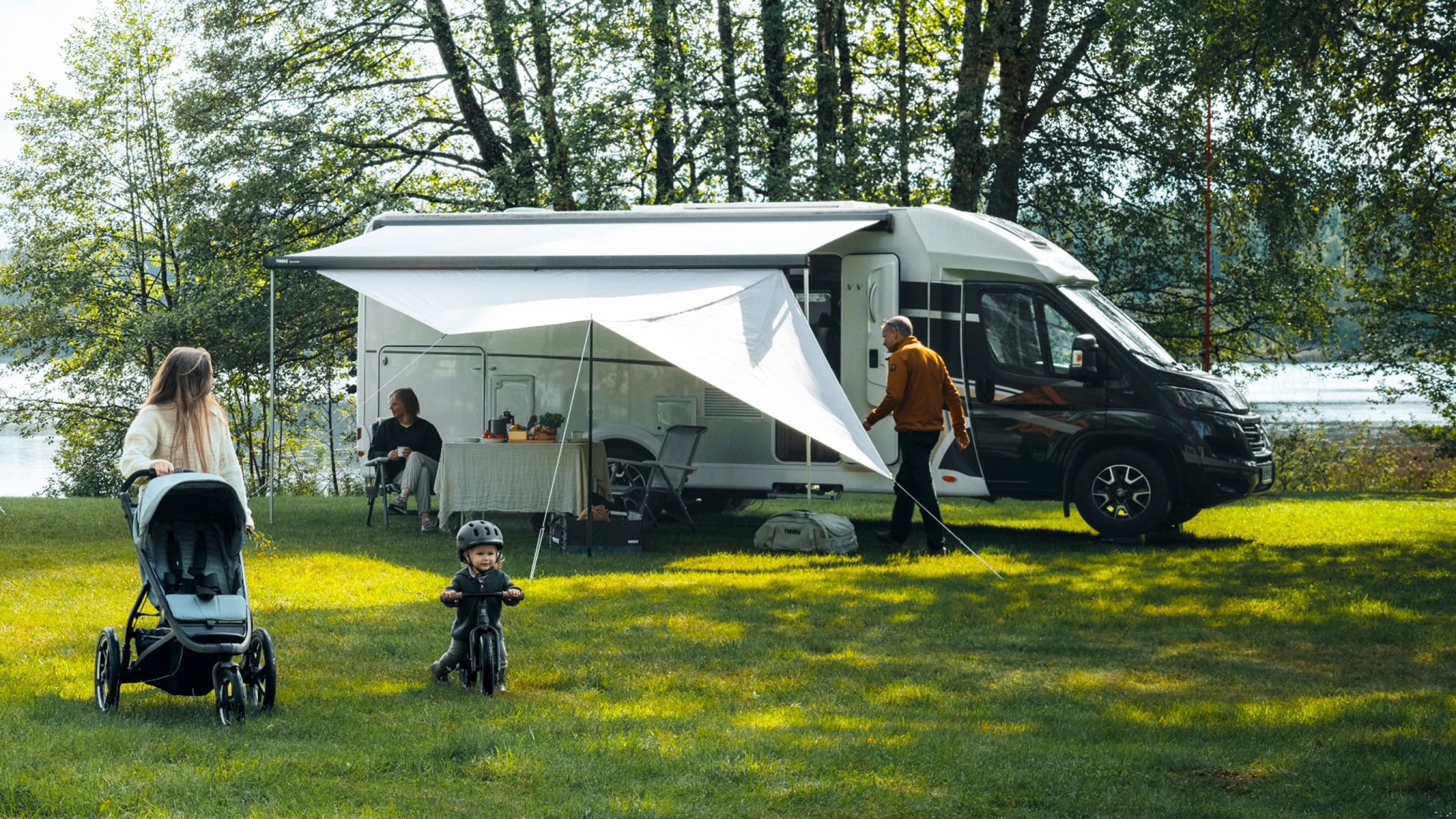 Camping familial avec un camping-car et des panneaux d’auvent Thule Subsola installés sur l’herbe.