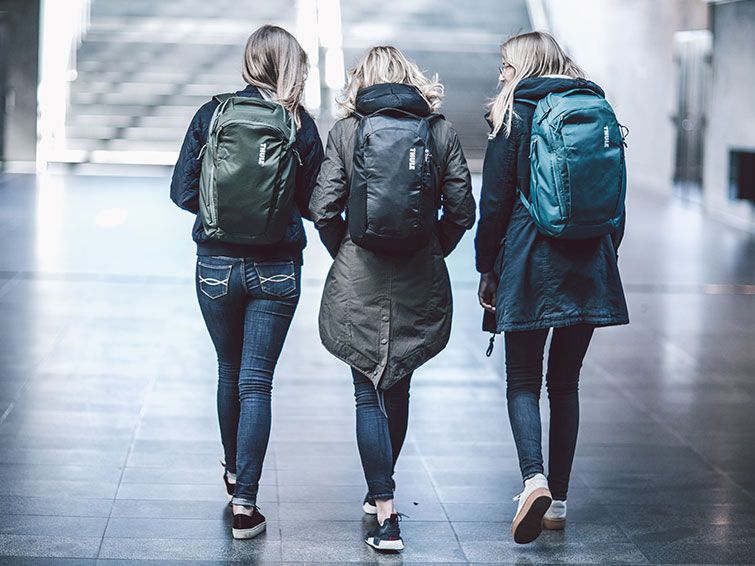 Three woman walk in a subway station with multicolored backpacks.
