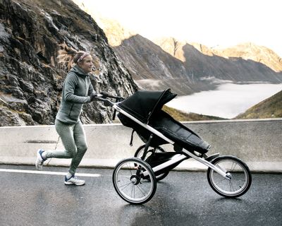 一位女士推着全地形轻便婴儿车在山下的街道上跑步。