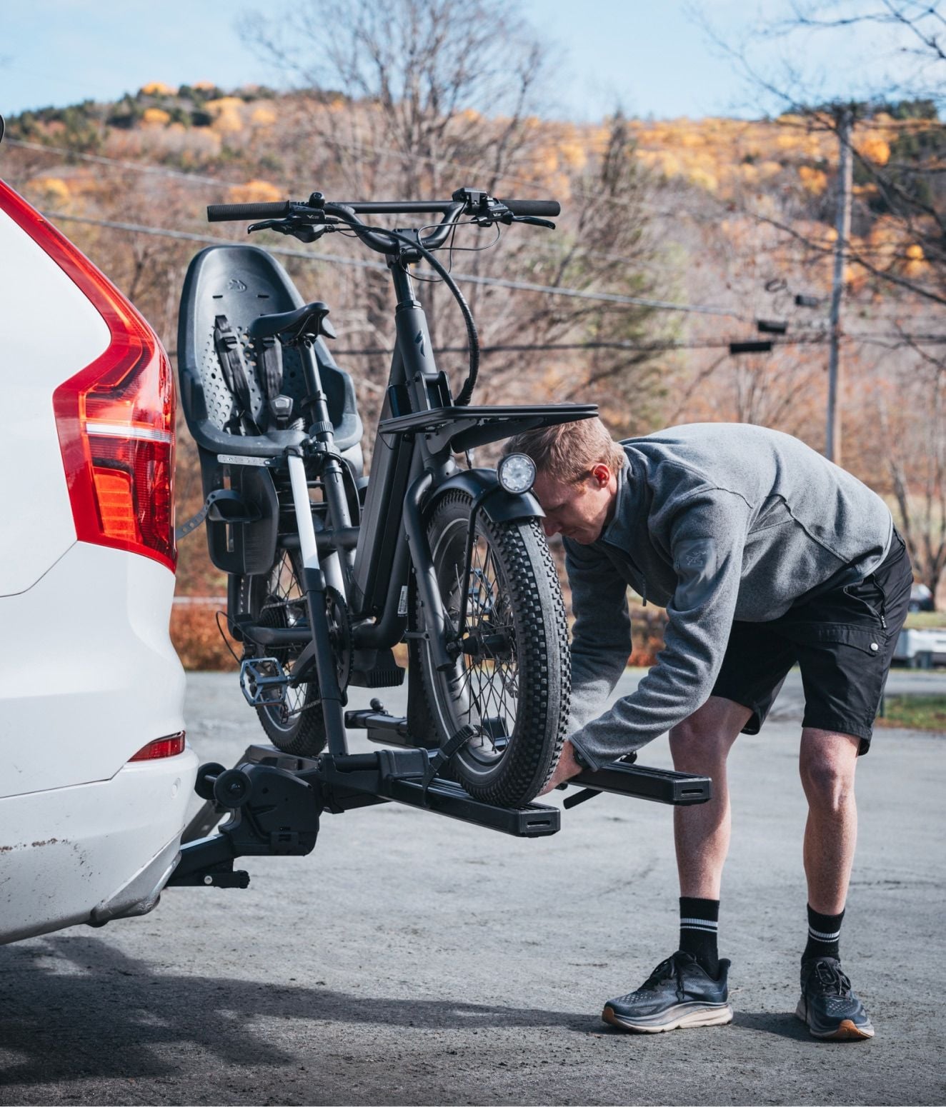 Man securing a bike onto a Thule Vero mounted on the back of a car outdoors.