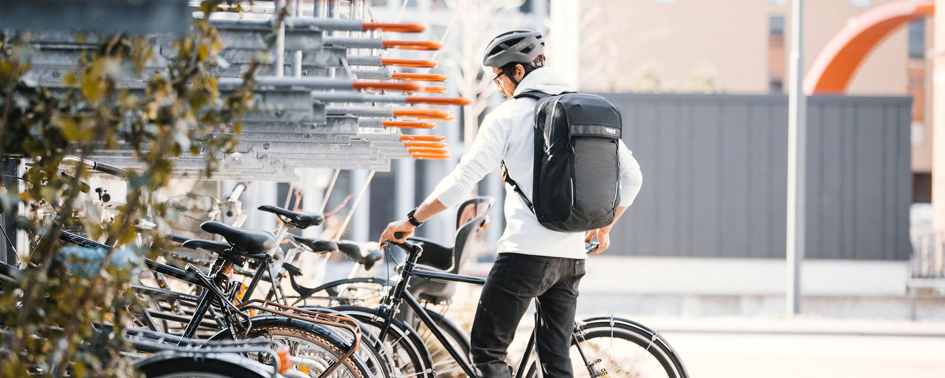 Man parks bike into a bike parking lot with a black Thule bike commuter backpack.