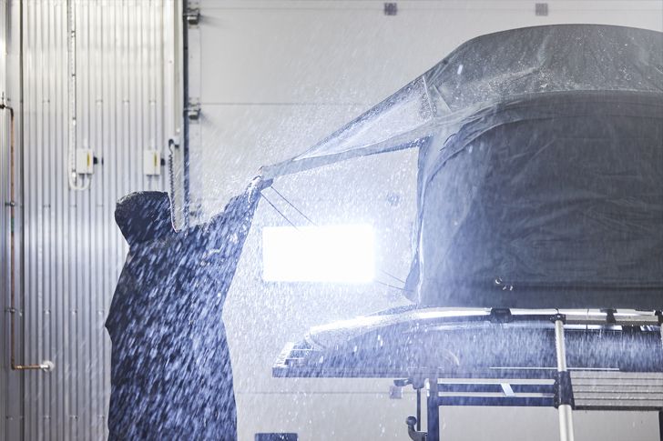 在 Thule Test Center，一位身穿雨衣的人在雨淋模擬期間，掀開了 Thule 車頂帳的護罩。
