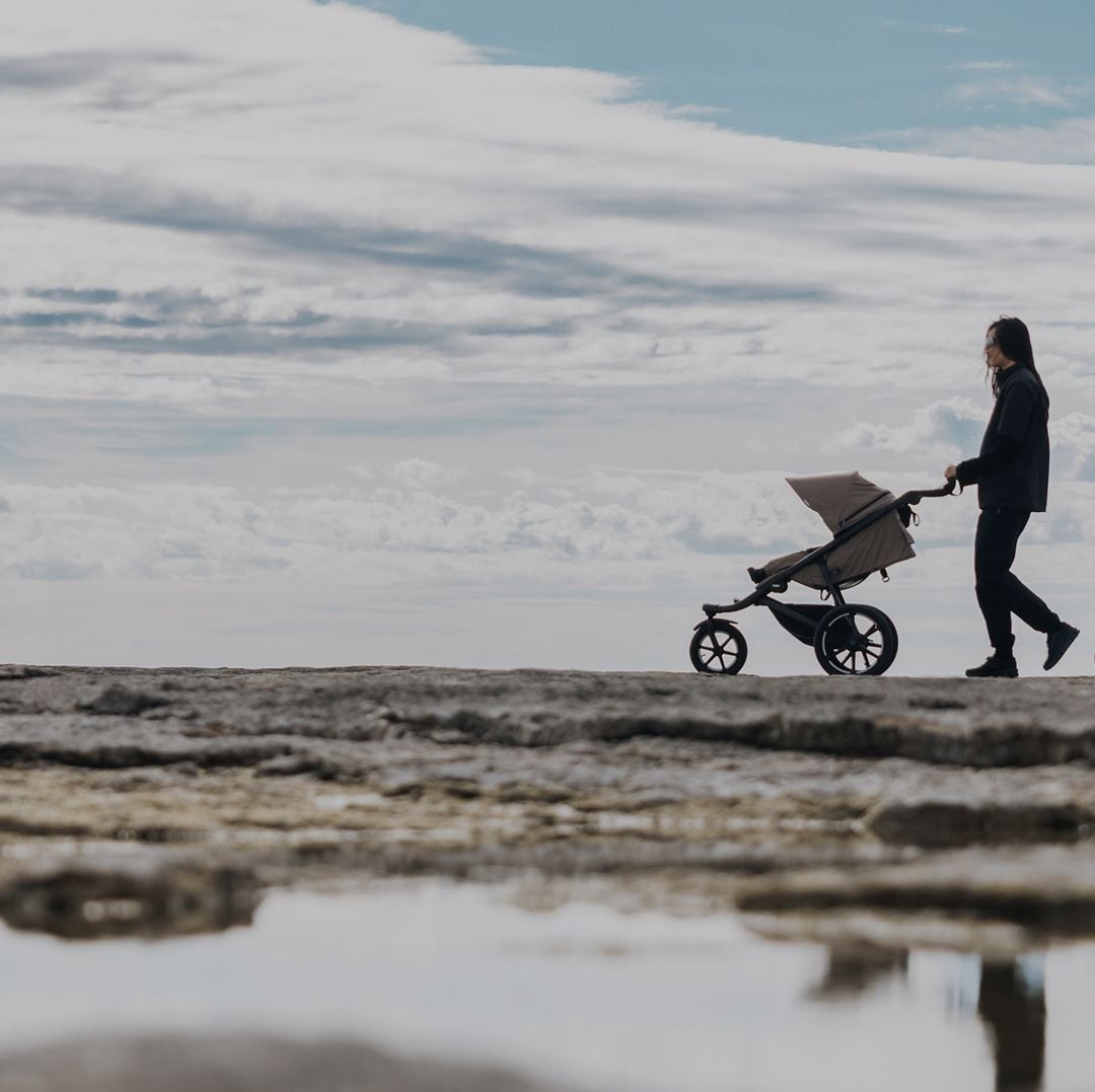 Two people walk along a rocky coastline with Thule Urban Glide strollers, showcasing their all-terrain design for outdoor adventures.