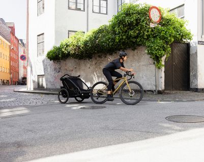 En person cykler, mens han trækker en børnetrailer på en stille bygade.