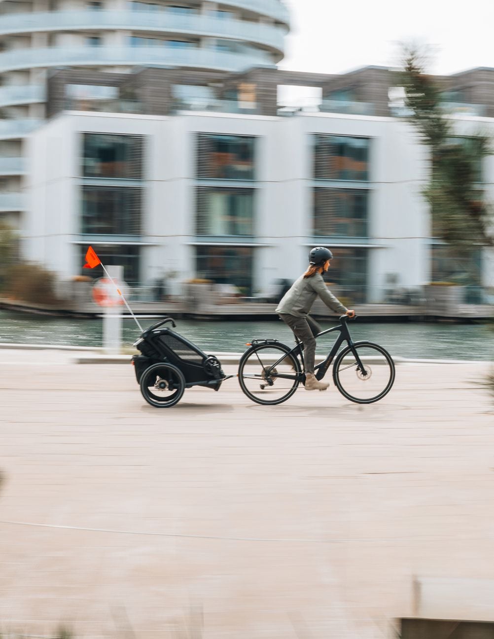 Personne faisant du vélo sur un chemin en bord de mer tout en remorquant une petite remorque de marchandises depuis Thulé.
