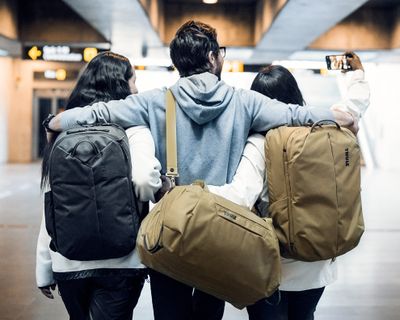 Three people take a selfie in the train station holding duffel bags.