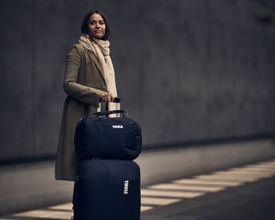 Kobieta stoi na dworcu kolejowym trzymając walizkę na kółkach.