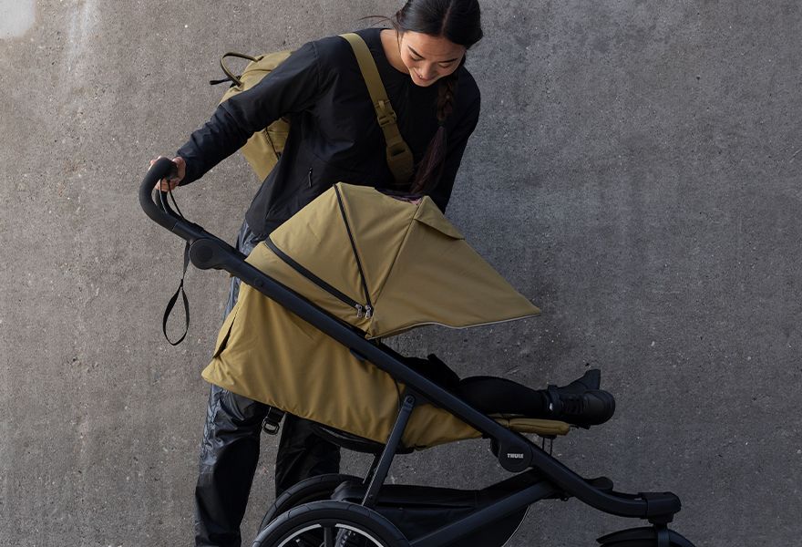 A woman checks on her child who is laying in a Thule Urban Glide 3 stroller.
