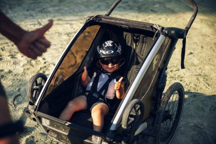Niño con casco sentado en una caravana de bicicletas en la playa haciendo un pulgar arriba.