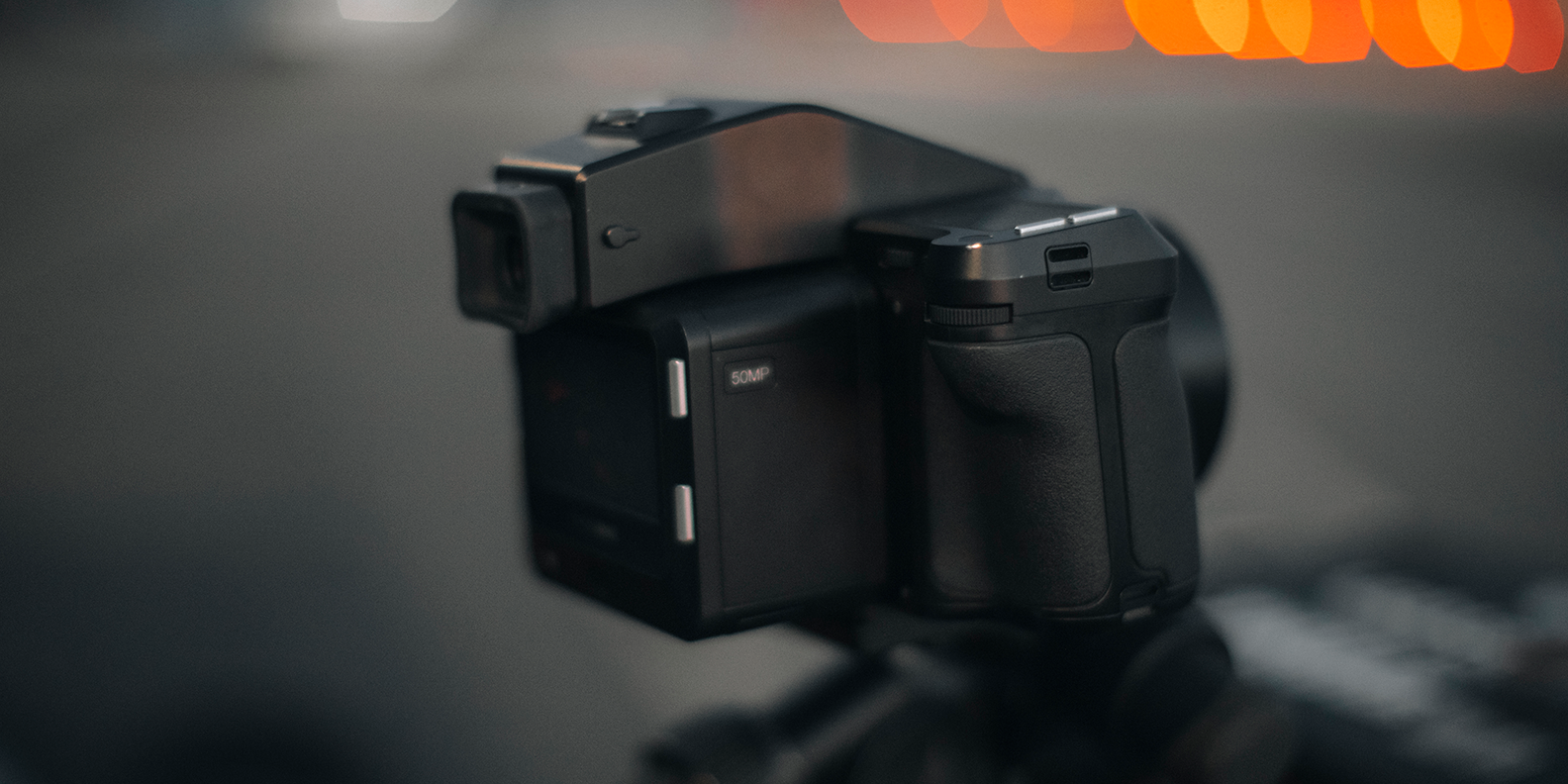 En digitalkamera på ett stativ, står redo att fotografera en mörk miljö med med varm ljus i bakgrunden.