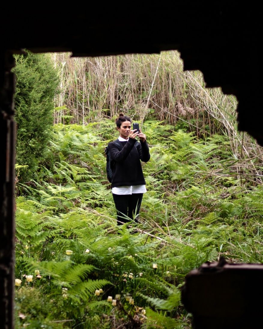 Maria Kuzma stands in some vegetation while taking a picture with her phone.