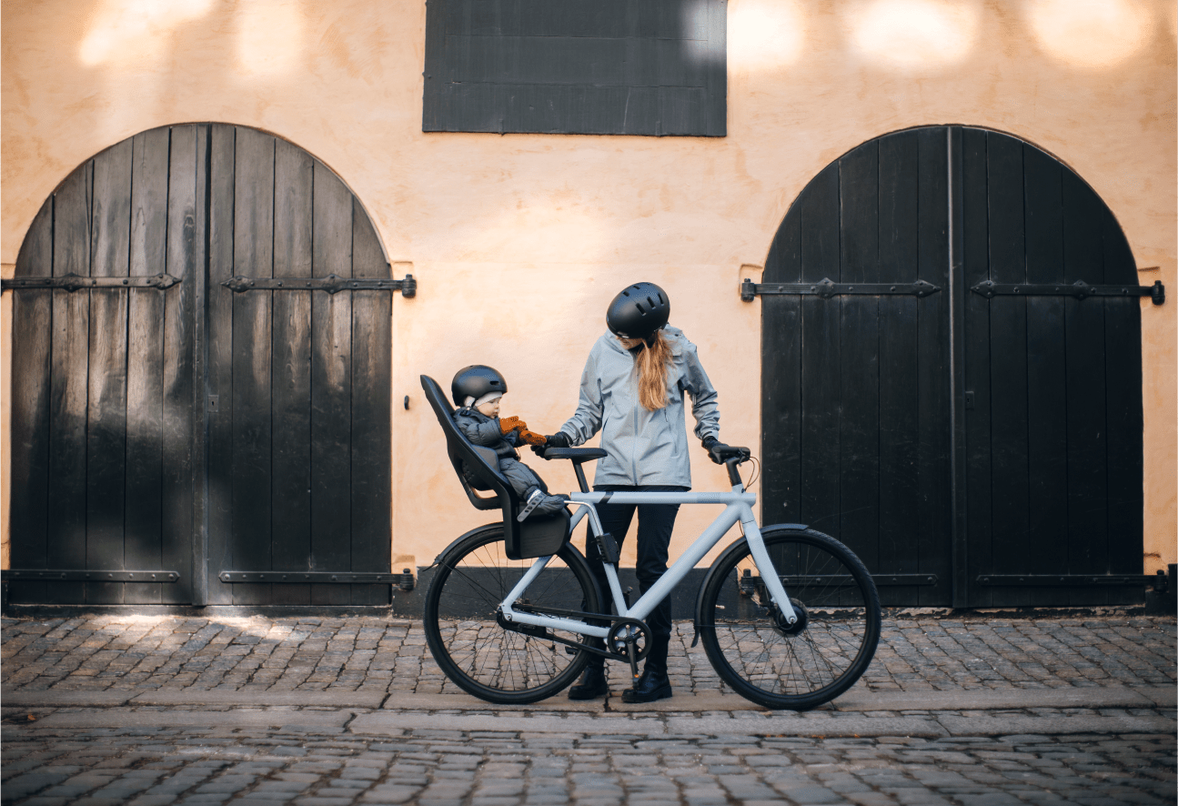 A woman tends to her baby in a Thule Yepp child bike seat next to a yellow wall.