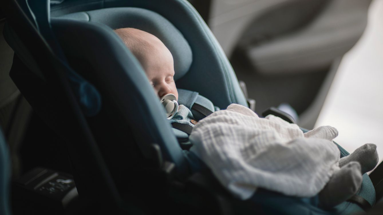 Um bebê dormindo em um assento infantil para veículos Thule Maple na traseira de um carro.