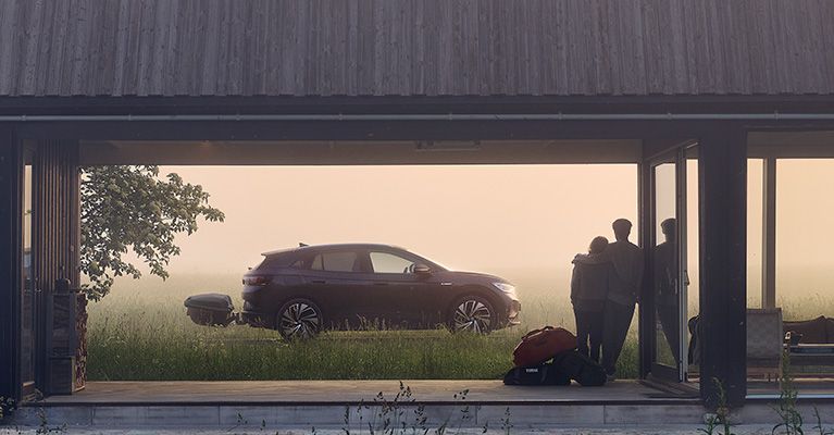 Una pareja mirando un coche estacionado en césped con neblina, con un cofre portaequipajes de bola de remolque Thule Arcos.