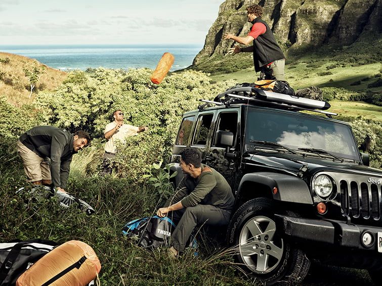 Four men have their jeep parked in the grass and unload bags from one of the Thule roof baskets.