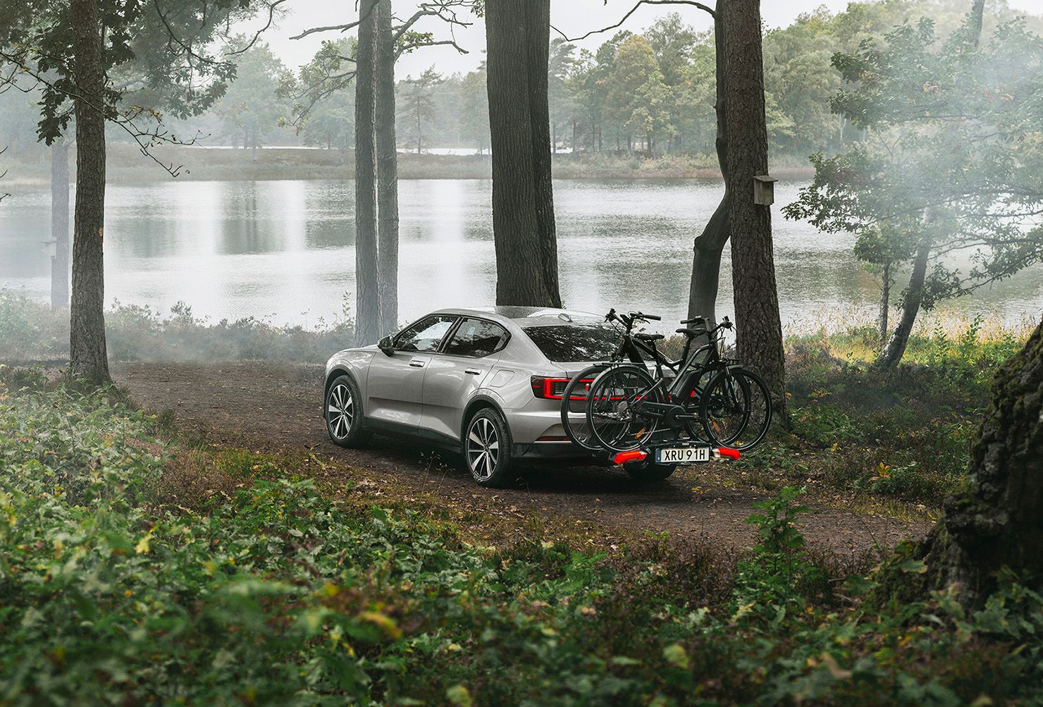 Une voiture est stationnée dans les bois près d’un lac avec un support pour vélos Thule Epos.