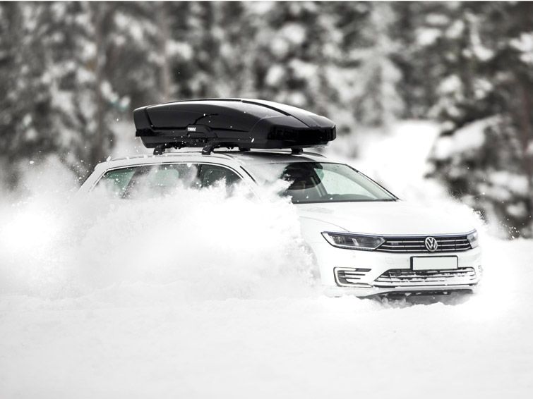 A car with a Thule Vector rooftop cargo carrier is parked in a snowy forest.