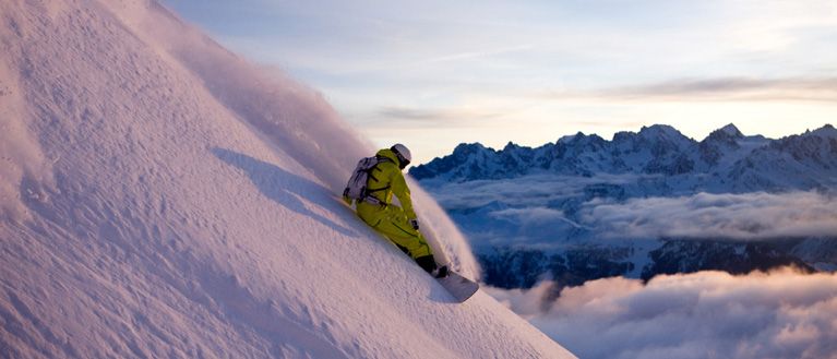 A skier skis down the steep slopes at Verbier, Switzerland at dawn, with rugged peaks in the background.